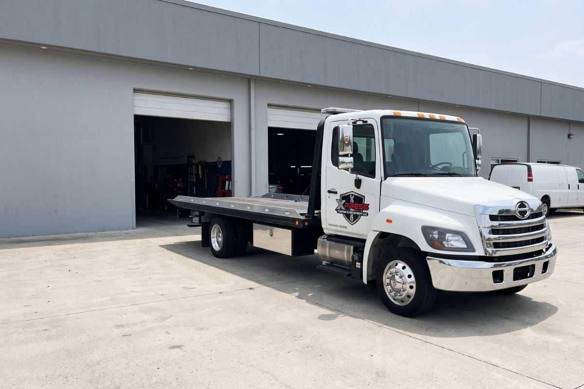 Xpress flatbed parked at the open bays of a repair shop, ready for a dealer pickup